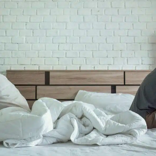 A man and a woman sit back-to-back on a bed, looking away from each other.