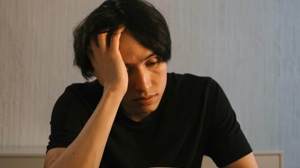 A man sitting with his hand on his head, looking tired or stressed.