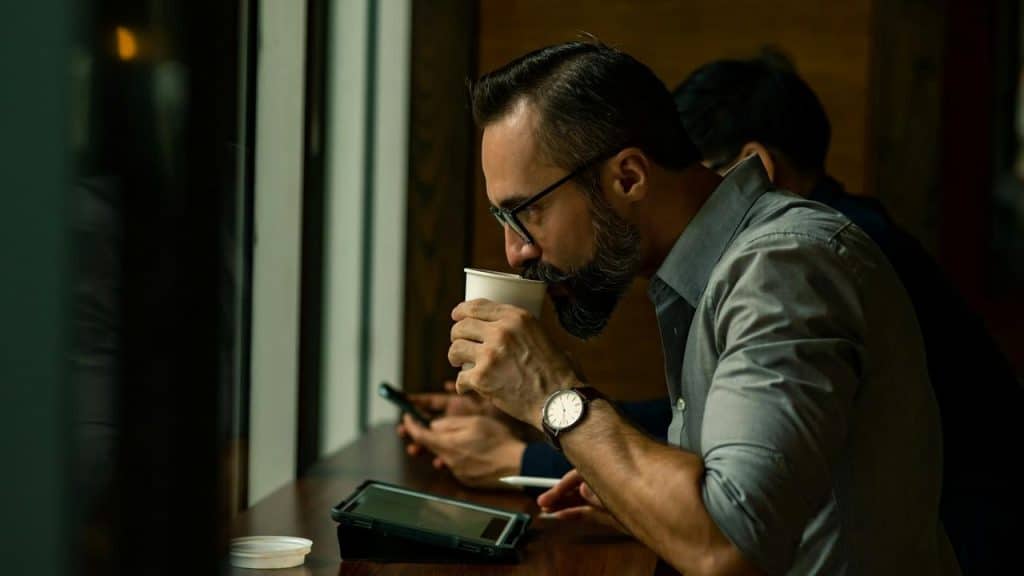 A man drinking coffee and using a tablet at a café counter.
