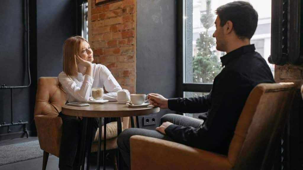 A man and woman sitting at a café table having coffee and talking.