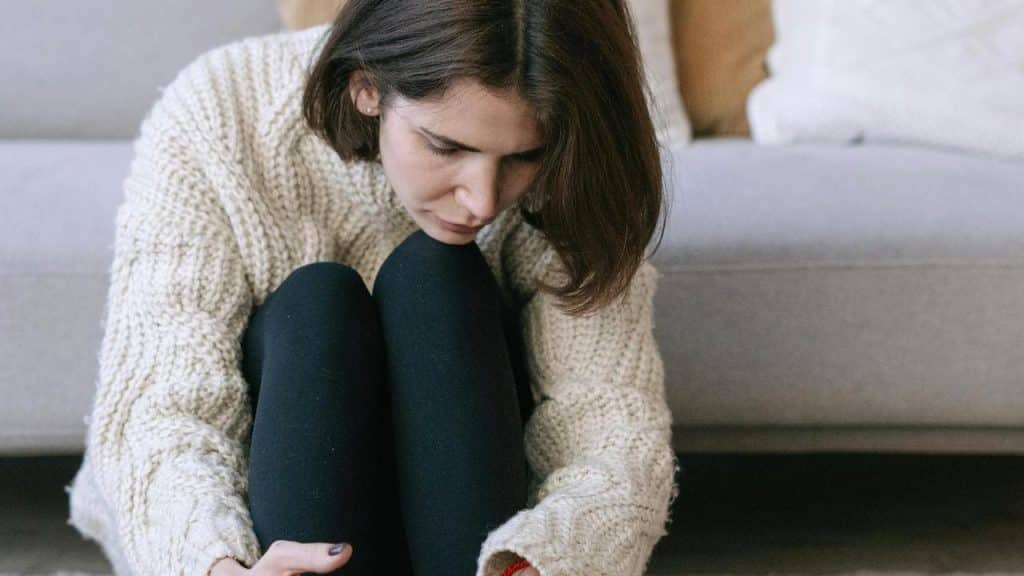 A woman sitting on the floor looking down.