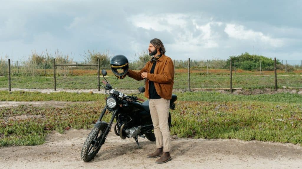 A man is standing next to a black motorcycle, holding a helmet outdoors.
