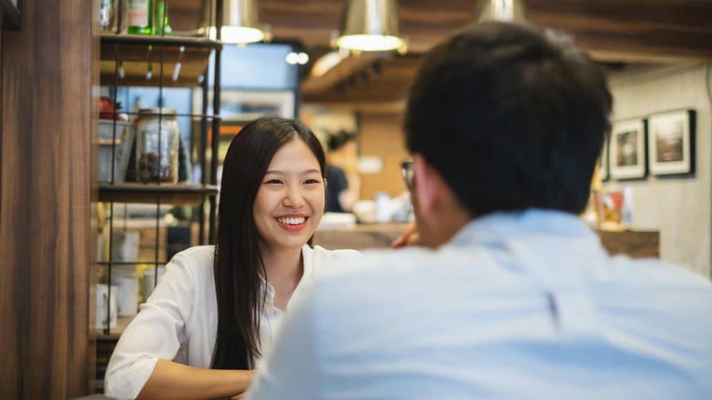 A woman smiling while talking with someone at a café table.