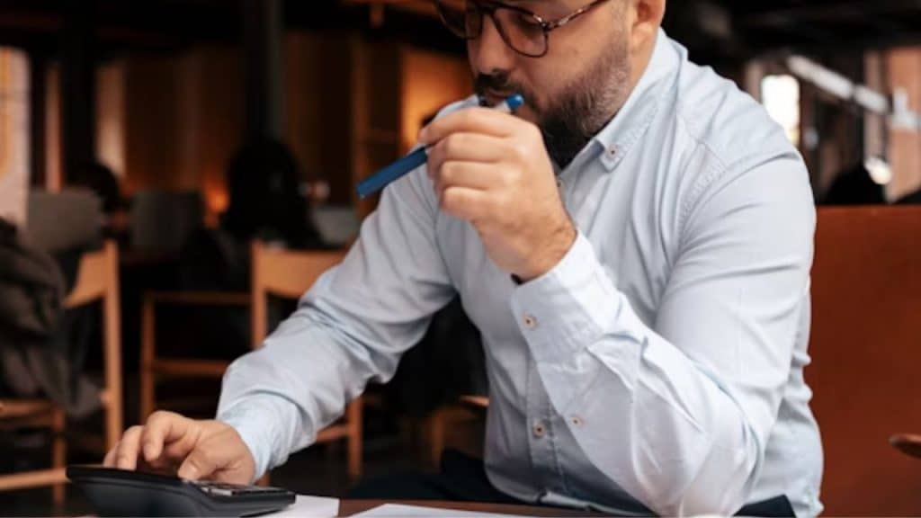Man reviewing bills at a kitchen table with a concerned look, warm evening light.
