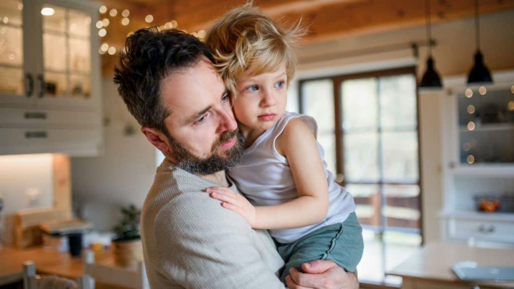 Man with a beard holding a young blonde child in a bright kitchen.