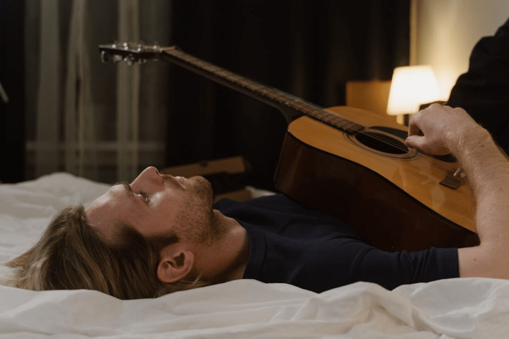 Man Lying in Bed Holding Acoustic Guitar