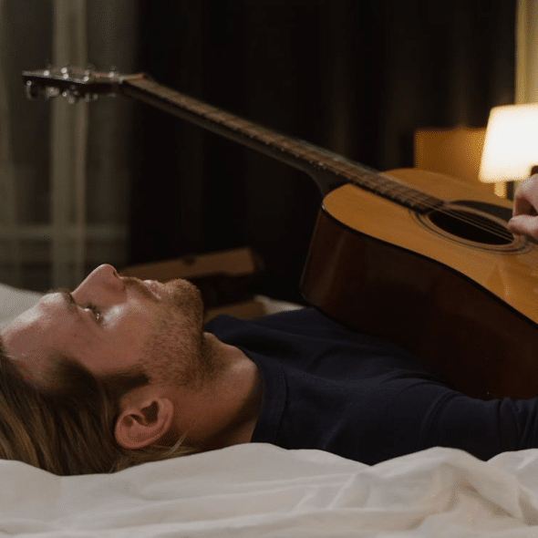 Man Lying in Bed Holding Acoustic Guitar