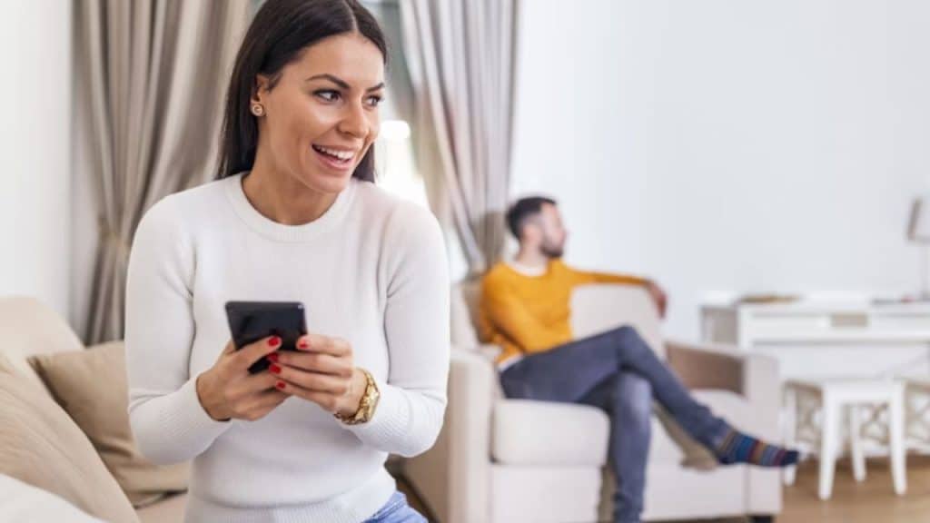 Woman texting while smiling as her partner looks away