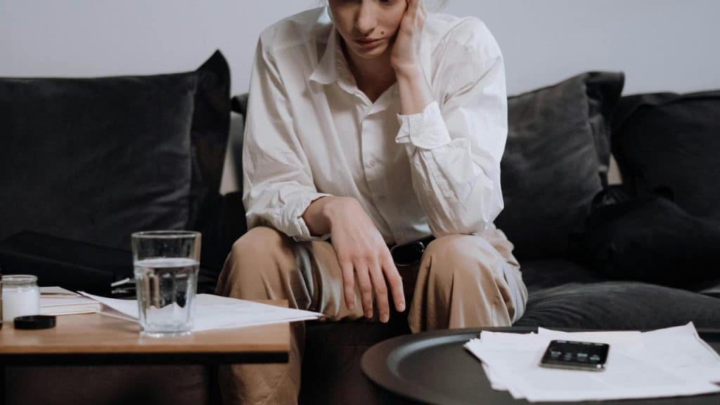 A woman sitting on a couch looking down at papers on a table.