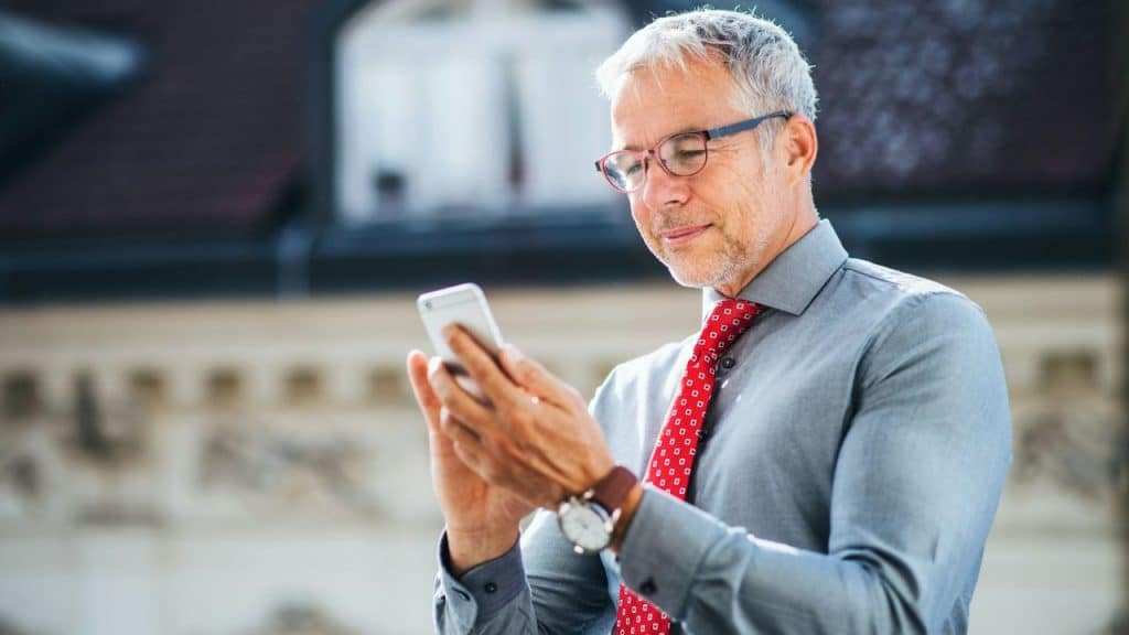 Mature man in a dress shirt and tie looks down at a white smartphone.