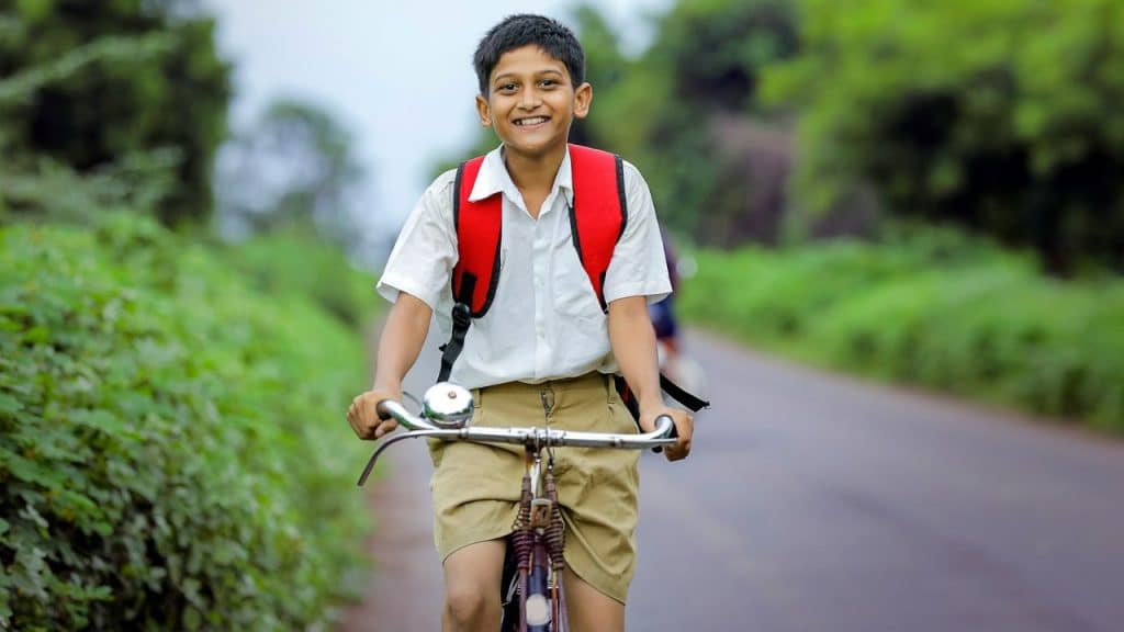 Smiling boy in a white shirt and shorts riding a bicycle on a rural road.