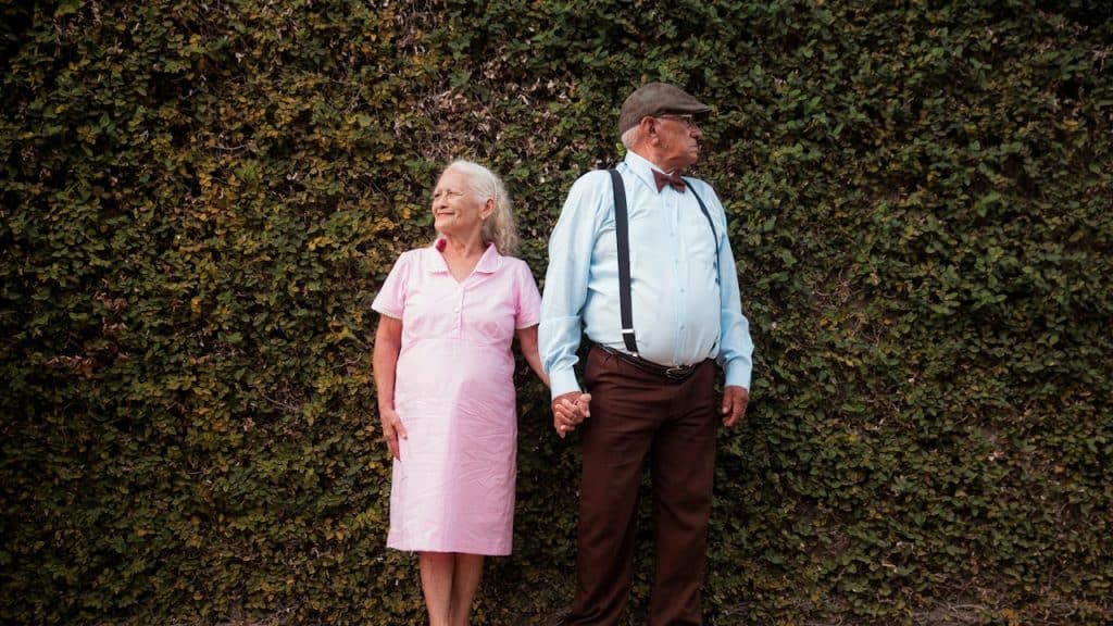 An old couple looking away from each other while holding hands.