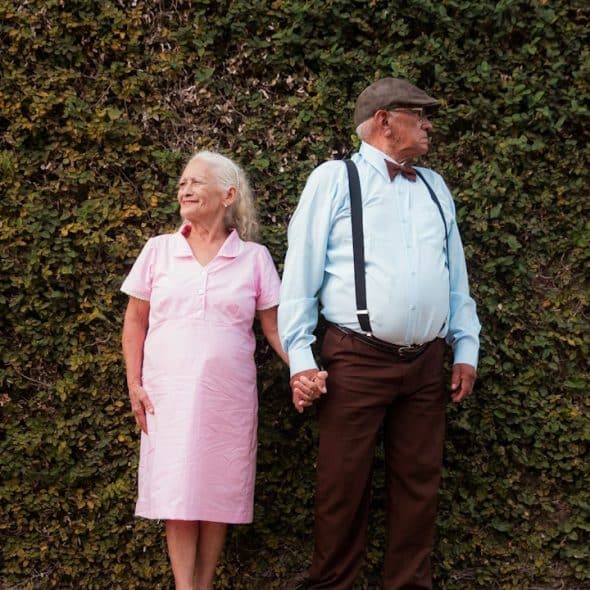 An old couple looking away from each other while holding hands.