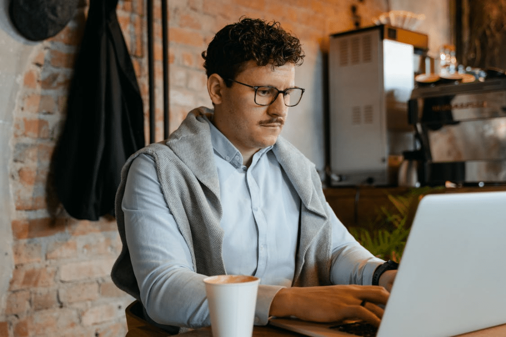 A Coffee Cup beside a Man Typing on Laptop