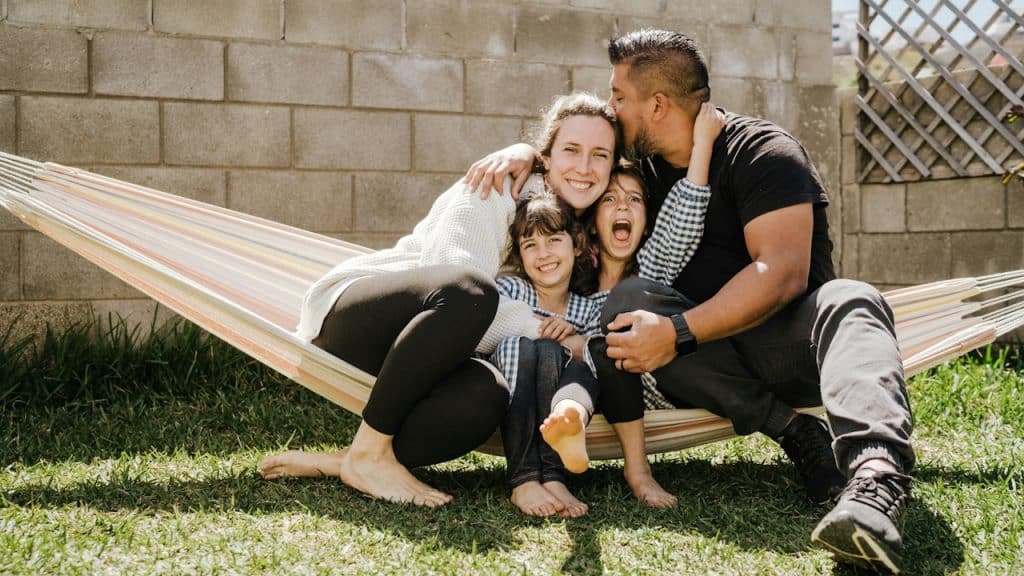 A family sitting on a hammock with the father kissing the mother.