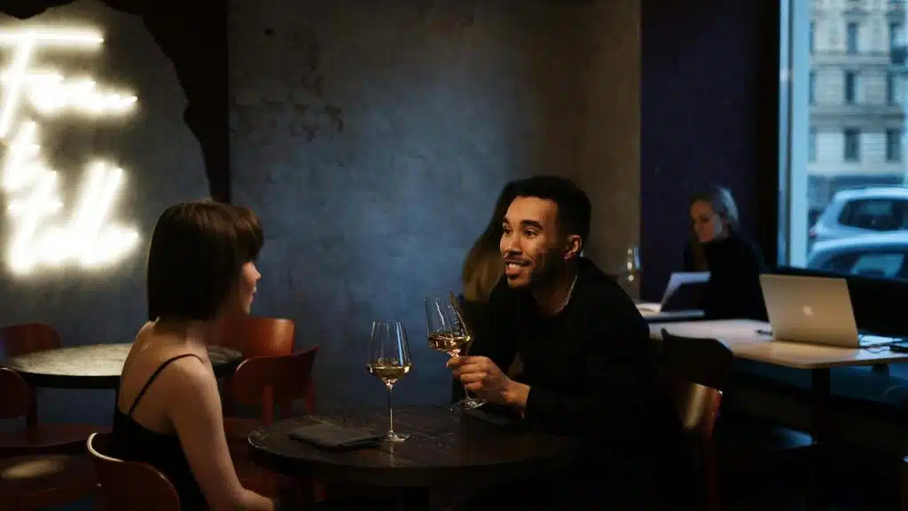 A man and woman having wine and talking at a restaurant table.