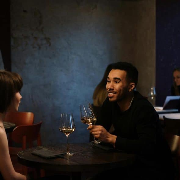 A man and woman having wine and talking at a restaurant table.