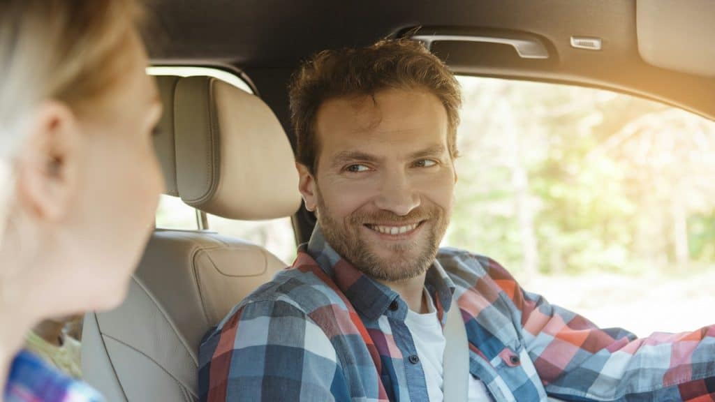 A man and a woman smiling at each other while sitting in a car.