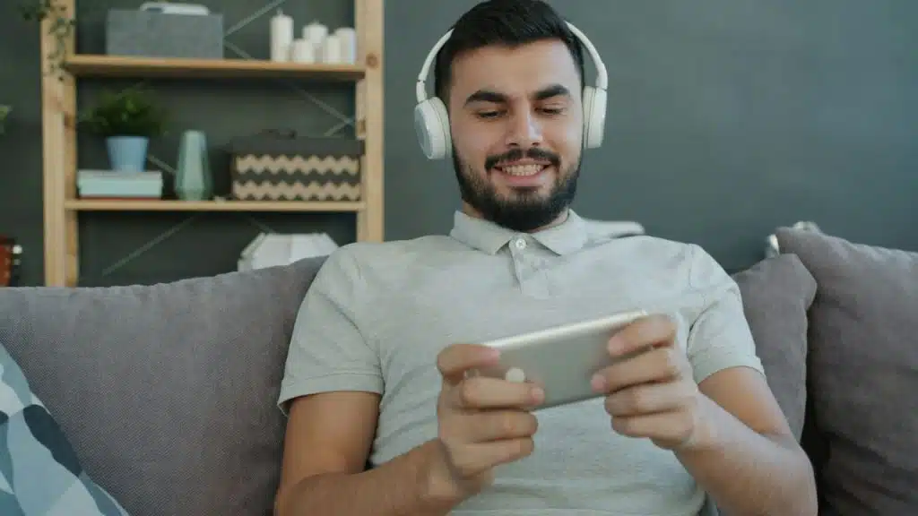 Smiling man on a couch with headphones is looking at his phone.