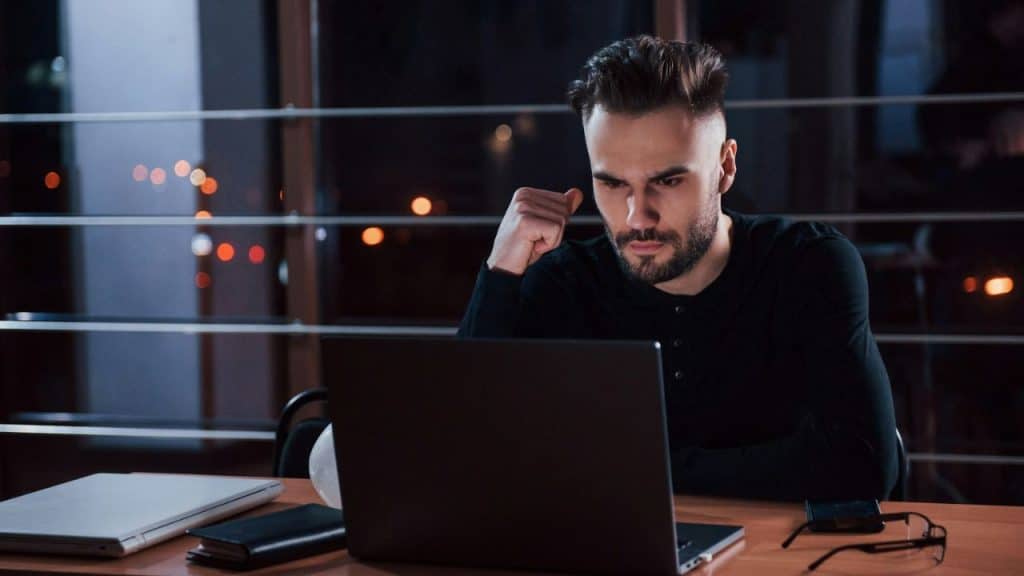 Man in a black shirt looking intently at a laptop at night.