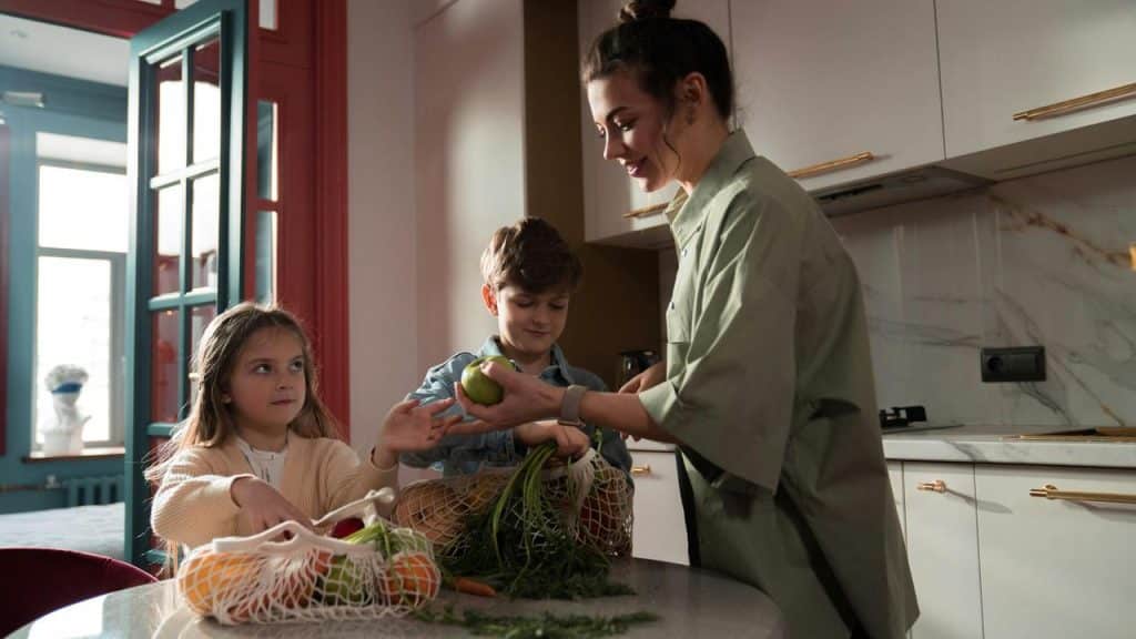 A woman and two children unpacking groceries in a kitchen.