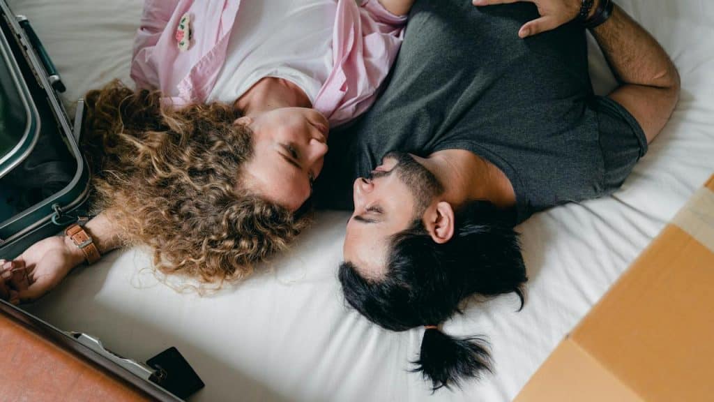A couple lying on a bed facing each other affectionately.