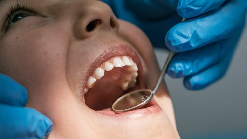 A close-up of a person's mouth wide open during a dental examination, with a gloved hand holding a dental mirror.