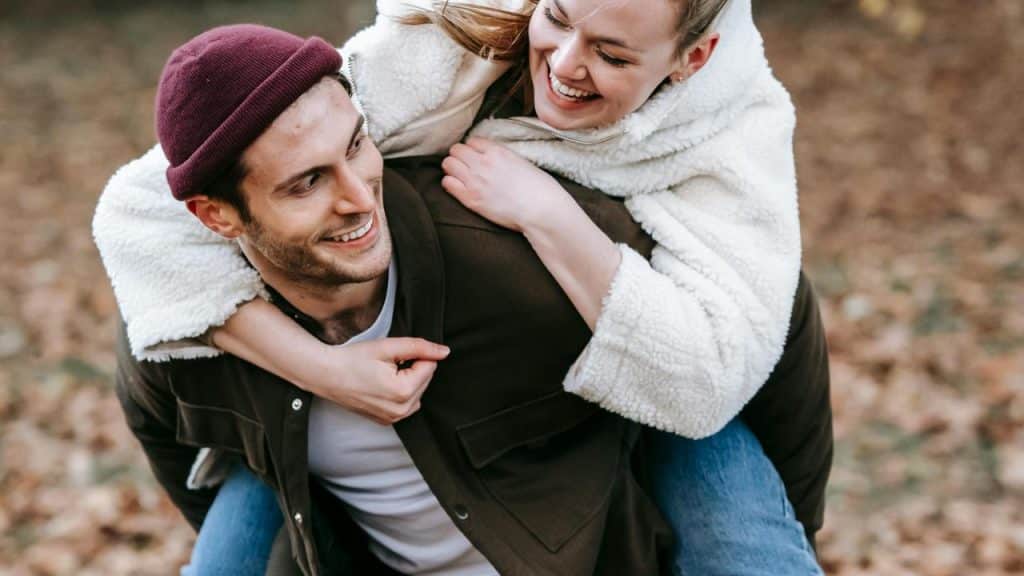 A man giving a woman a piggyback ride while both are smiling outdoors.