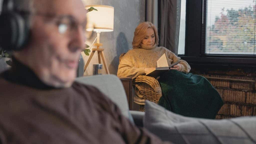 A woman reading a book while a man listens with headphones in the foreground.