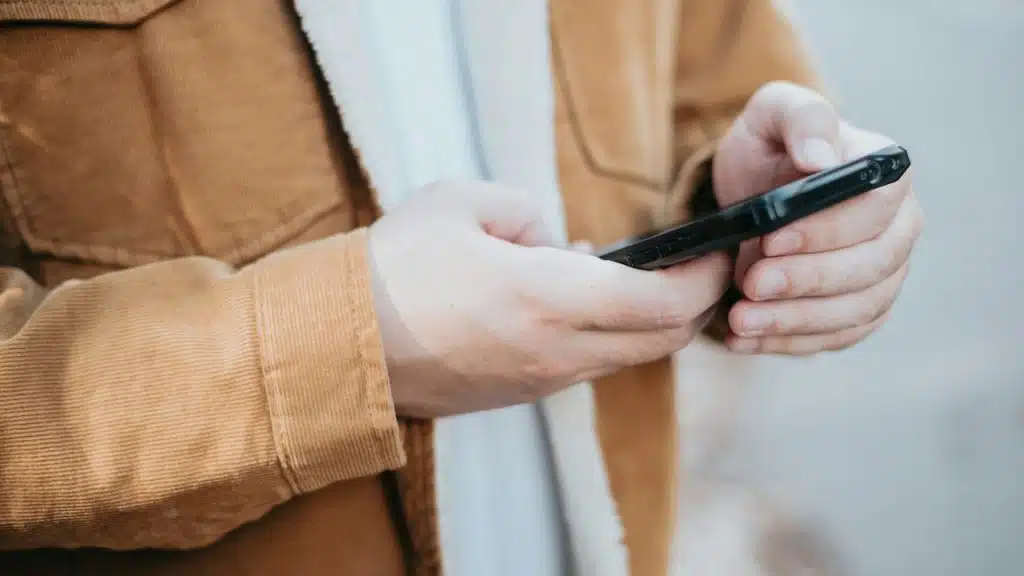 Close-up of a person wearing a tan corduroy jacket with a sherpa lining, holding and using a black smartphone.