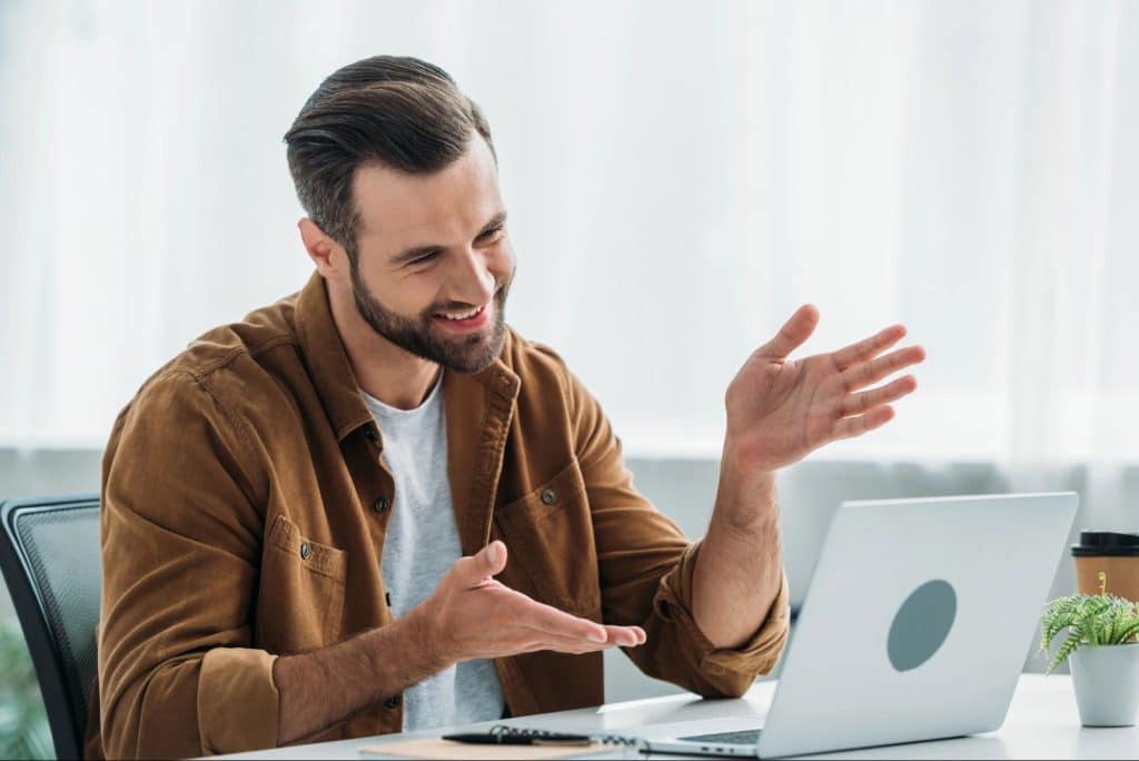 The man is looking at the laptop screen while smiling.