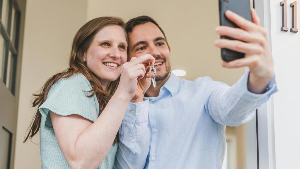 A smiling couple taking a selfie while holding house keys.