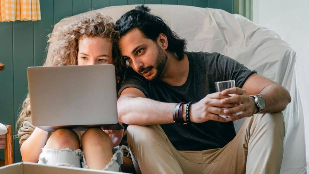 A couple sitting on the floor looking at a laptop together.