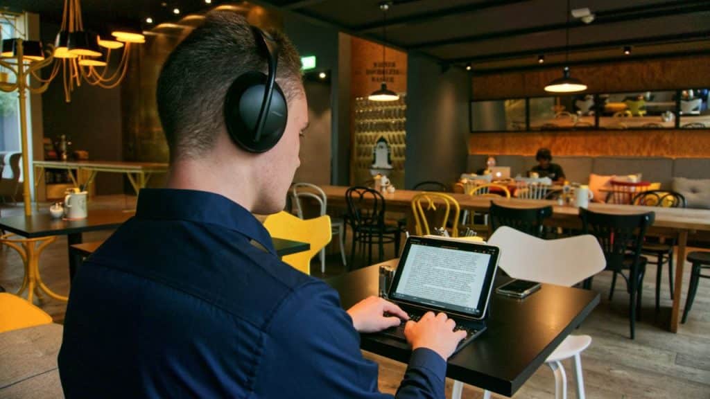 Man wearing headphones and typing on a tablet keyboard in a busy restaurant or cafe.