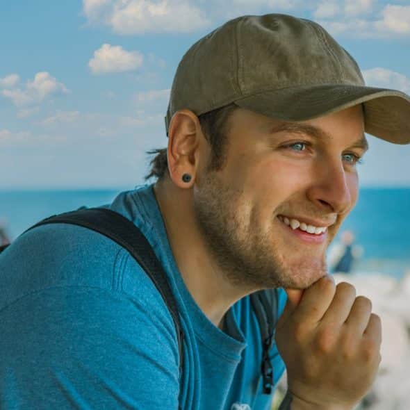 A man wearing a cap hanging out at a beach and smiling.