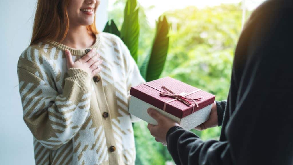 A boyfriend surprising and giving his girlfriend a gift box.