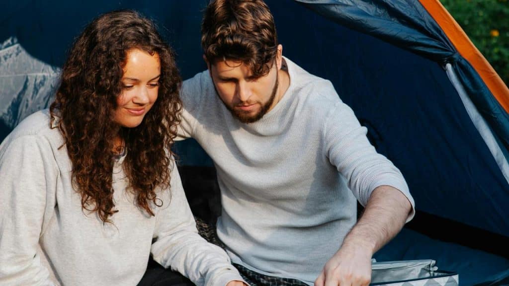 A couple sitting together at a campsite, preparing something.