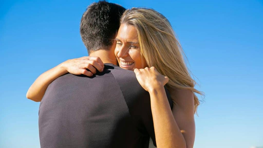 A smiling woman hugging a man under a clear blue sky.
