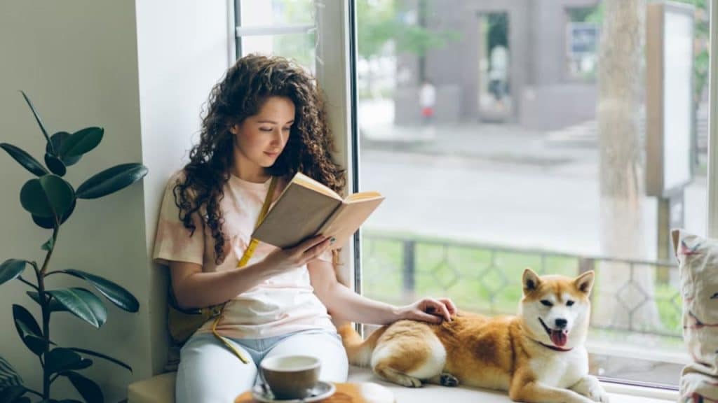 A thoughtful woman by the window, reading with soft natural light.