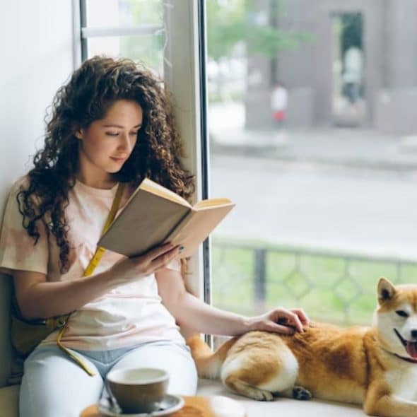 A thoughtful woman by the window, reading with soft natural light.