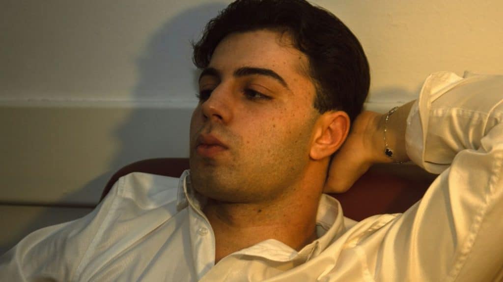 Young man in a white collared shirt leaning back with his hand behind his head.