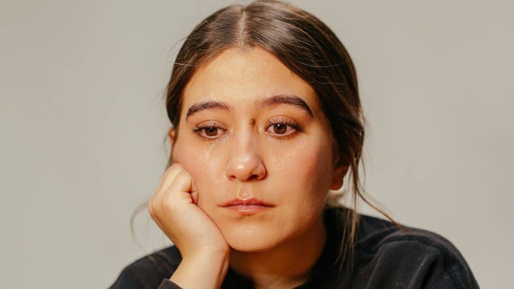A woman with brown hair rests her chin on her hand, with a tear rolling down her cheek.