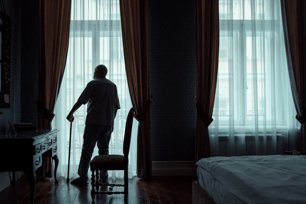 Back View of an Elderly Man Standing in Front of the Window