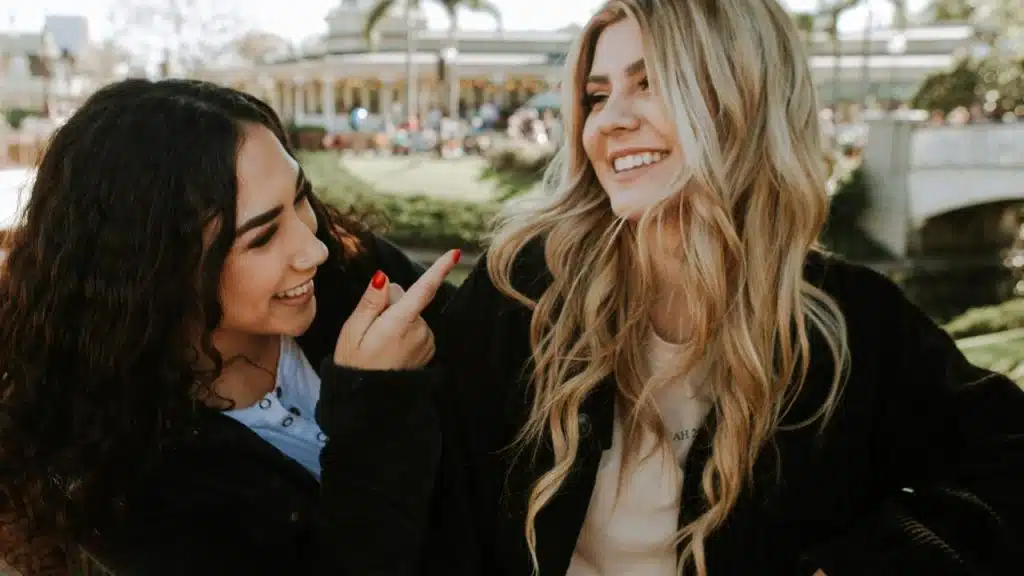 A woman smiling and pointing at her friend outdoors.