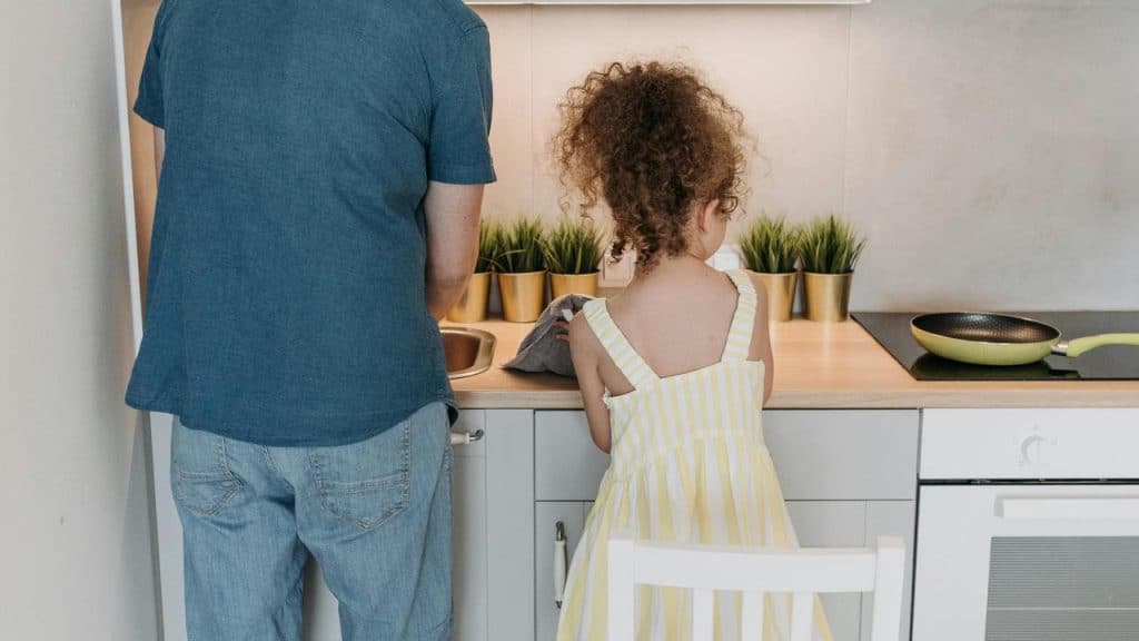 A man and a young girl standing at a kitchen counter washing dishes together.