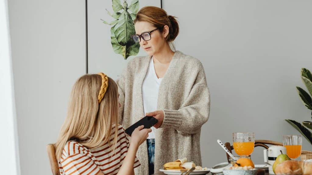 A mother taking a phone from her daughter at the breakfast table.