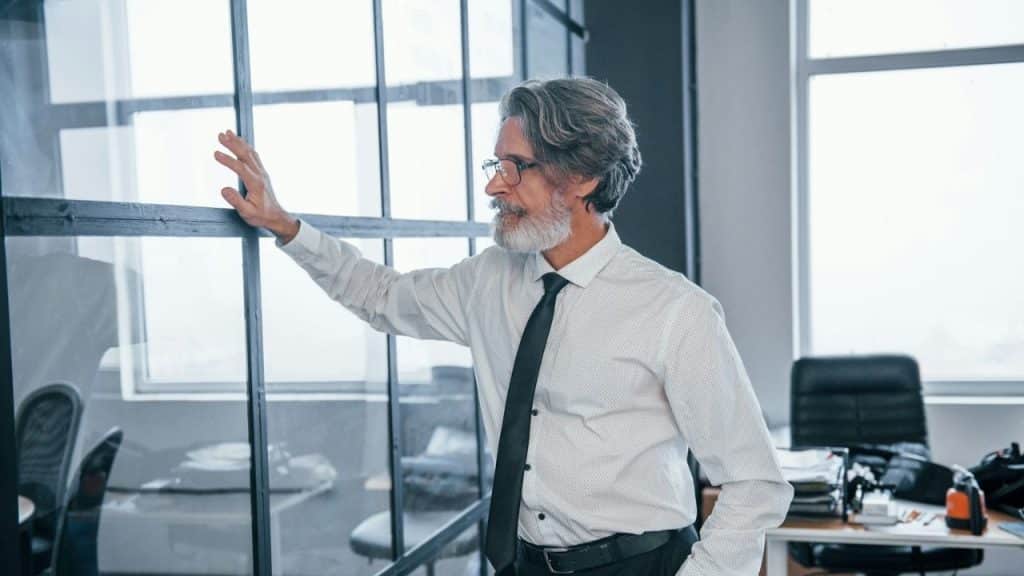 Mature man in an office shirt and tie with a hand on a glass partition.