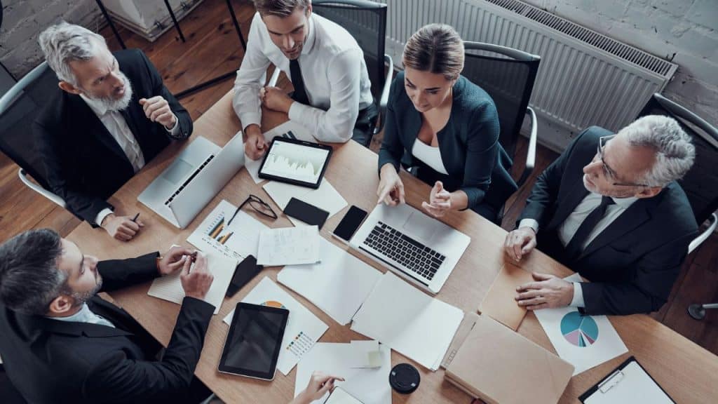 Overhead shot of five business people in suits having a discussion at a table.
