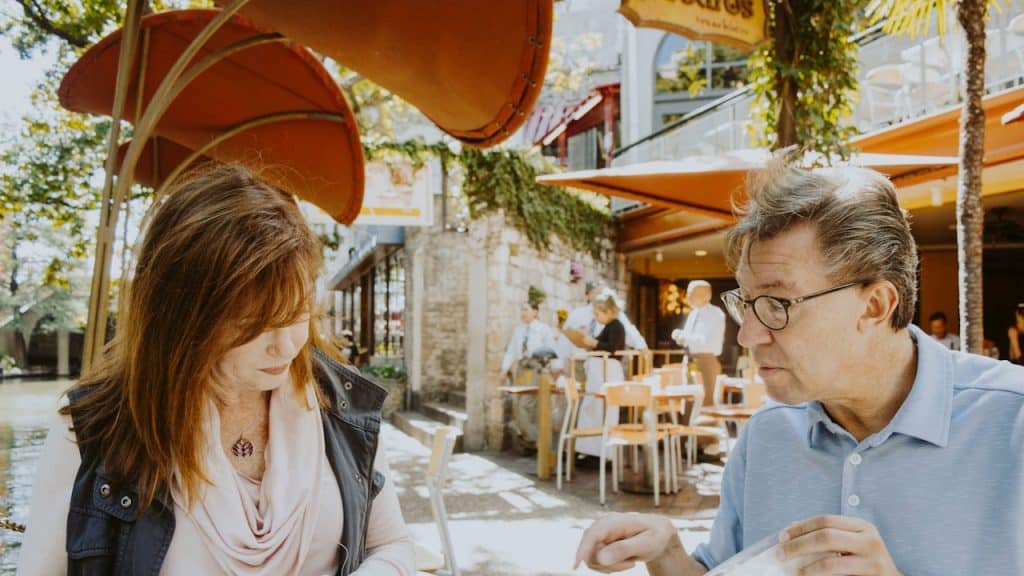 A couple sitting at an outdoor cafe on a sunny day, both looking intently at the menus on the table.