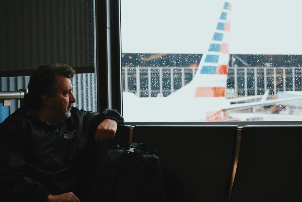 The man is sitting in the airport and looking at the airplane outside.